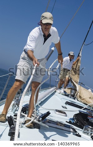 Sailors working ropes on deck of a yacht against clear blue sky and sea