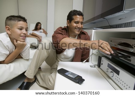 Father with son putting disc in DVD player in living room at home