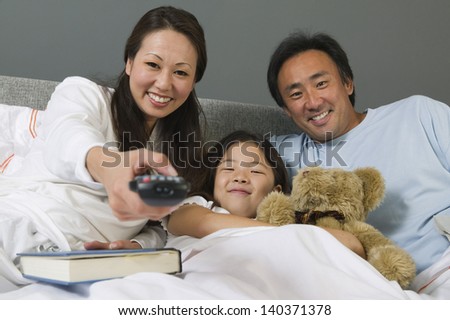 Family watching TV together in bed while mother using remote control at home