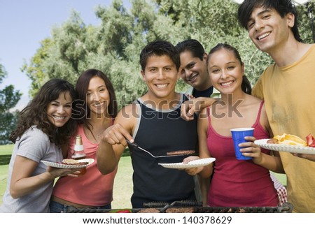 Group portrait of young people gathered around the grill at picnic