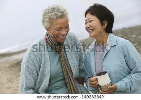 Two Cheerful Middle Aged Female Friends Talking On The Beach
