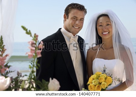 Portrait of happy bride and groom with flowers against the ocean