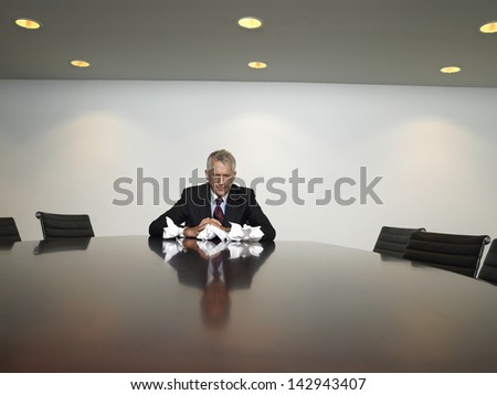 Sad businessman with crumpled paper balls at table in conference room