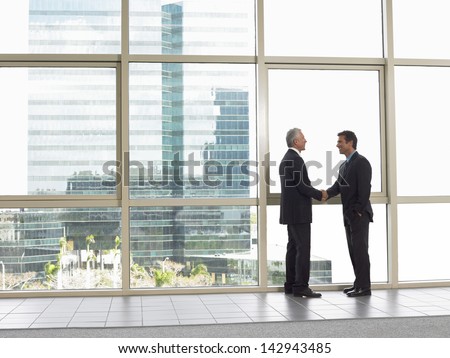 Full length side view of businessmen shaking hands in office building