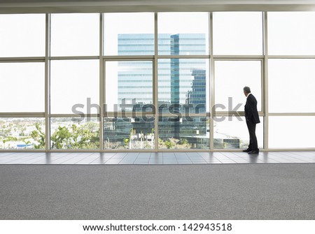 Full length of businessman looking out of office window Full length of businessman looking out of office window