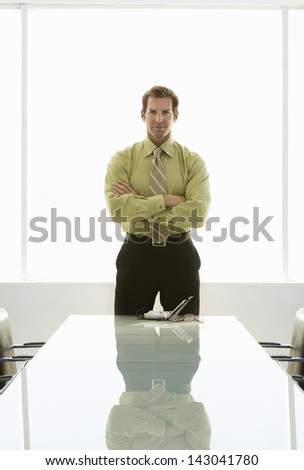 Portrait of confident businessman with arms crossed standing at conference table