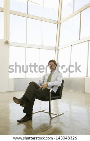 Full length of young businessman sitting on armchair in empty conference room