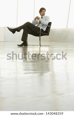 Full length of young businessman sitting on armchair in empty conference room