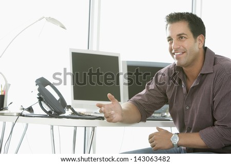 Confident businessman gesturing with computers and landline phone on office desk