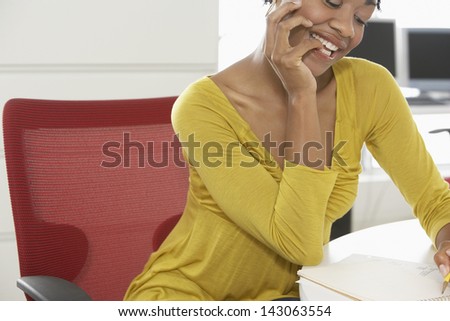 Happy African American woman writing on notepad at office desk