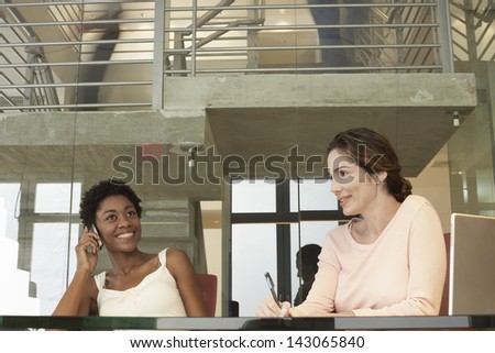 Happy African American businesswoman using mobile phone with female colleague in conference room