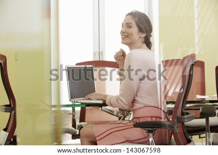 Happy young businesswoman using laptop in meeting room