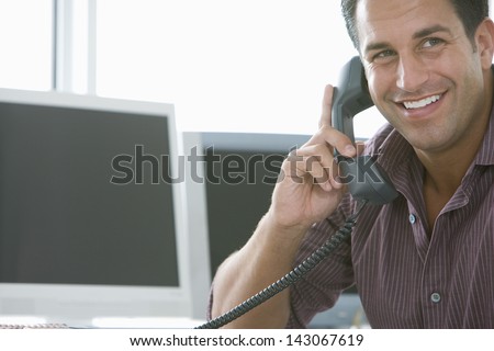 Smiling businessman using landline phone in office