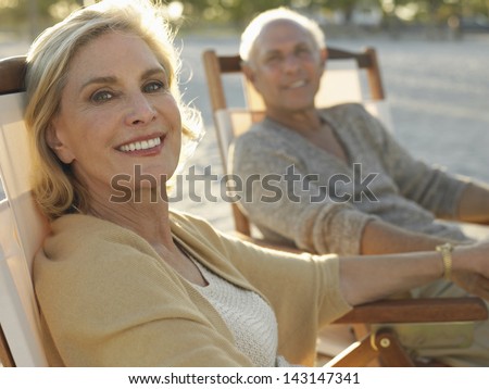 Portrait Of Happy Middle Age Woman With Man Relaxing On Deckchairs At Beach