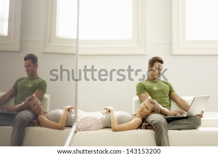 Young man using laptop with woman lying on his lap at home