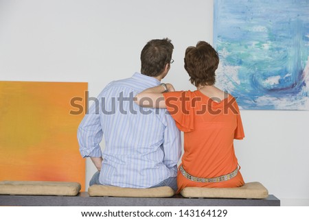 Rear view of couple observing painting while sitting on bench in art gallery
