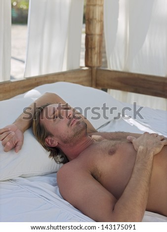 Thoughtful young man lying in four-poster bed on beach