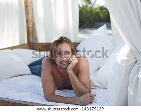 Portrait of thoughtful young man lying in four-poster bed on beach