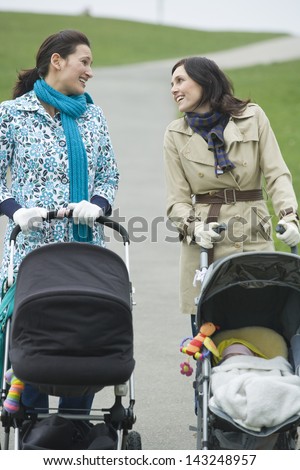 Happy young mothers pushing strollers in park having chat