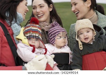 Cheerful Young Mothers With Babies In Slings Chatting Outdoors