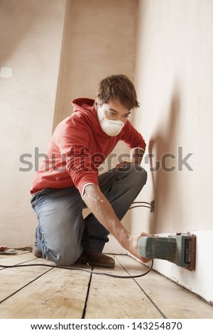 Full length of man wearing mask while sanding wall in unrenovated room