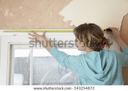 Rear View Of Woman Measuring Window Frame With Tape In Unrenovated House