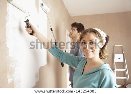 Portrait of woman and man painting wall with paint rollers