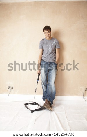 Full length portrait of man dipping paint roller in paint at unrenovated house