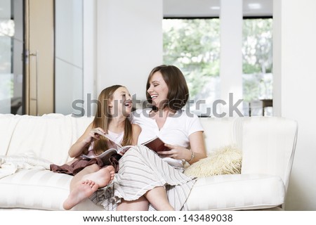 Cheerful Mother And Daughter Reading Book In Living Room