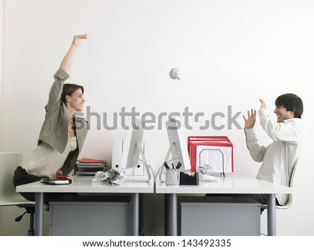 Side View Of Mischievous Businesswoman Throwing Paper Ball On Male Executive Over Desks