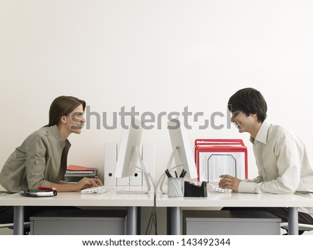 Side view of smiling business people using computers at office desks