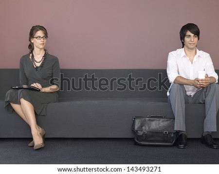 Full length of young businessman and businessman sitting on sofa in waiting room