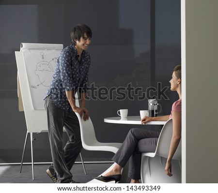 Young businessman giving presentation on flipchart to female colleague in meeting room