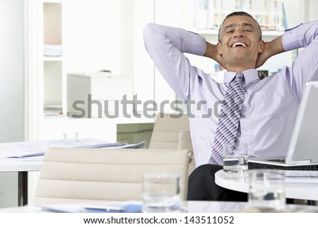 Cheerful middle aged businessman relaxing with hands behind head at office desk