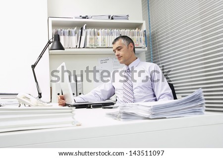 Middle aged businessman using laptop with paperwork at office desk