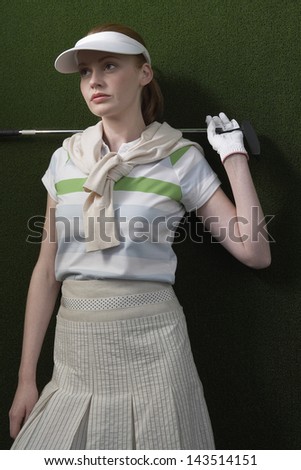 Young woman holding golf club behind shoulders against green background