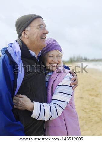 Smiling senior couple in winter clothing embracing at beach