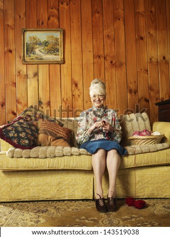 Full Length Portrait Of Senior Woman Sitting On Sofa Knitting At Home