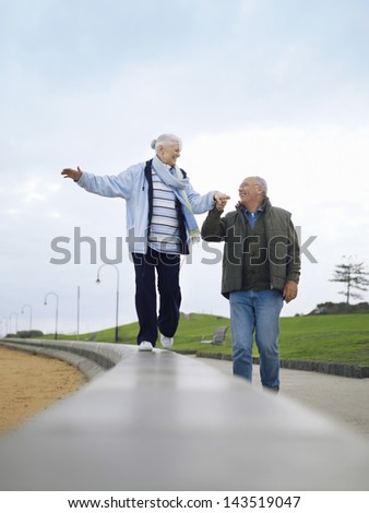 Happy senior couple walking on wall holding hands outdoors