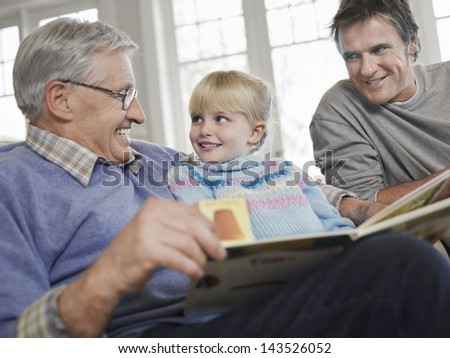 Young girl with father and grandfather reading story book at home