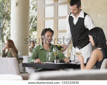 Waiter serving wine to young couple at outdoor restaurant