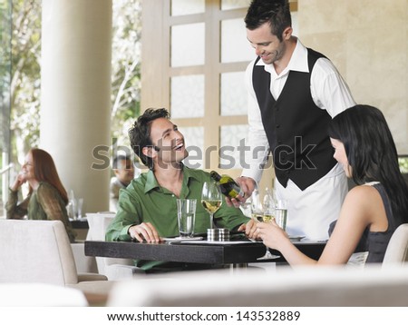 Waiter Serving Wine To Young Couple At Outdoor Restaurant