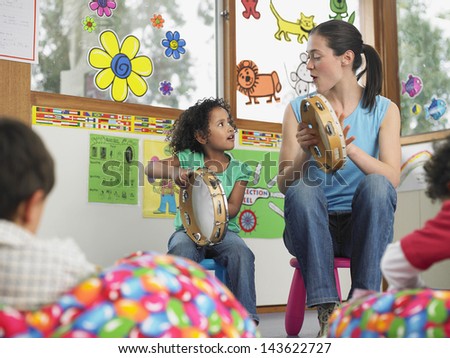 Young Teacher With Girl Playing Music In Classroom