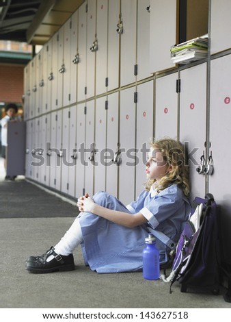 Side view of elementary girl sitting on floor against school lockers