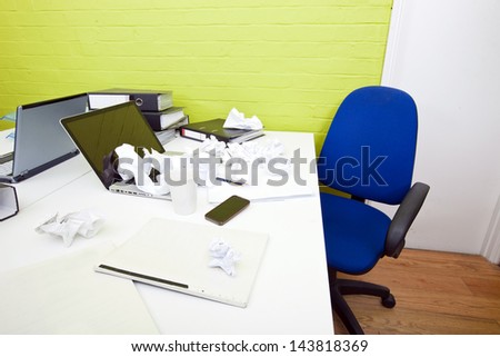Crumpled paper over laptop on desk with empty chair and folders