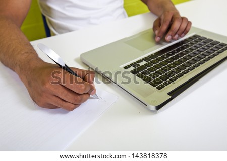 Close up of Indian mans hands writing on paper next to laptop