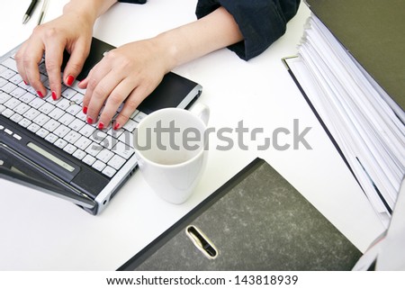 Close up of woman's hands typing on laptop with folders and mug
