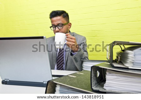 Portrait of Indian Businessman holding mug and working on his laptop computer at his desk
