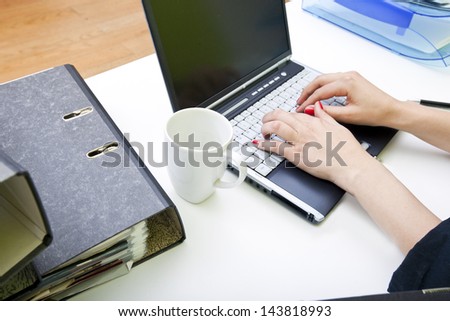 Close up of woman\'s hands typing on laptop with folders and mug