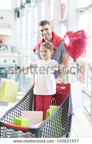 Father pushing young daughter in shopping trolley with shopping bags